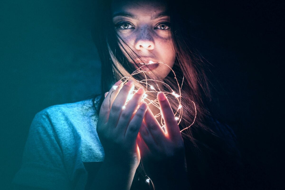 Moody portrait of a woman holding glowing string lights in the dark. Captivating and artistic.
