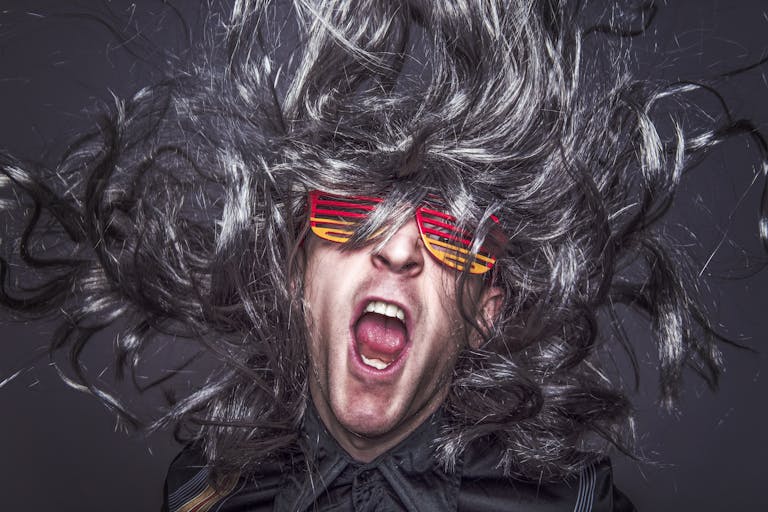 Vibrant portrait of a man with wild hair and colorful sunglasses expressing energy and fun.
