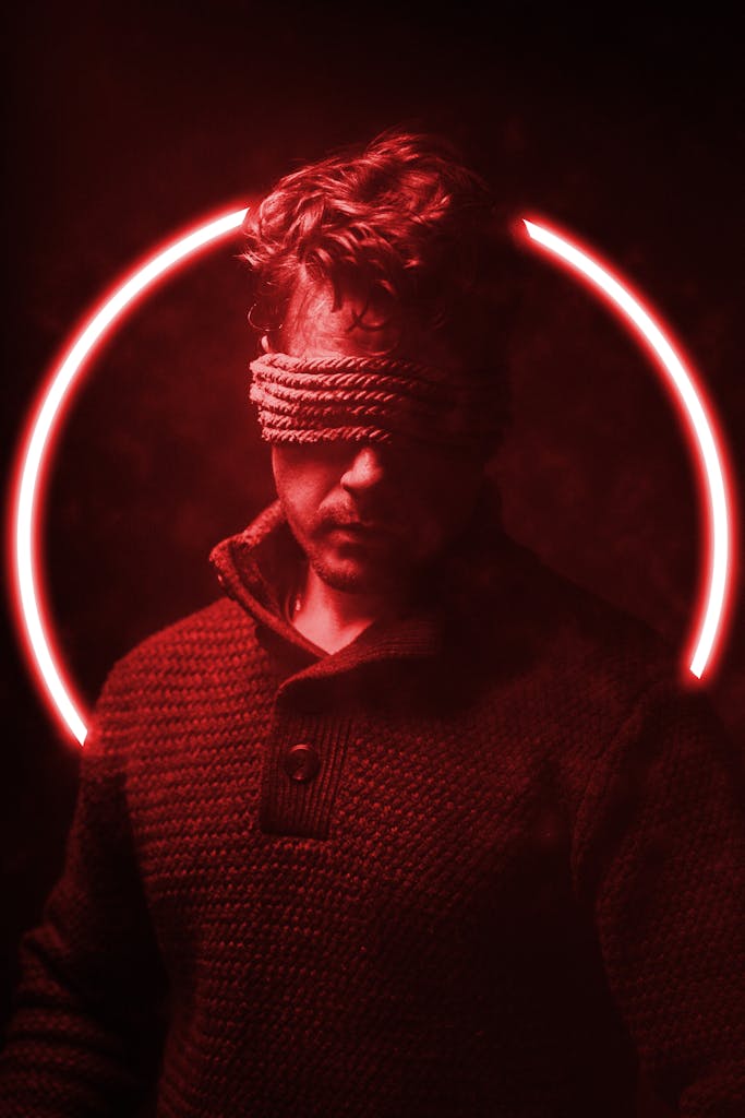 A man blindfolded, surrounded by red light and smoke, creating a dramatic atmosphere.