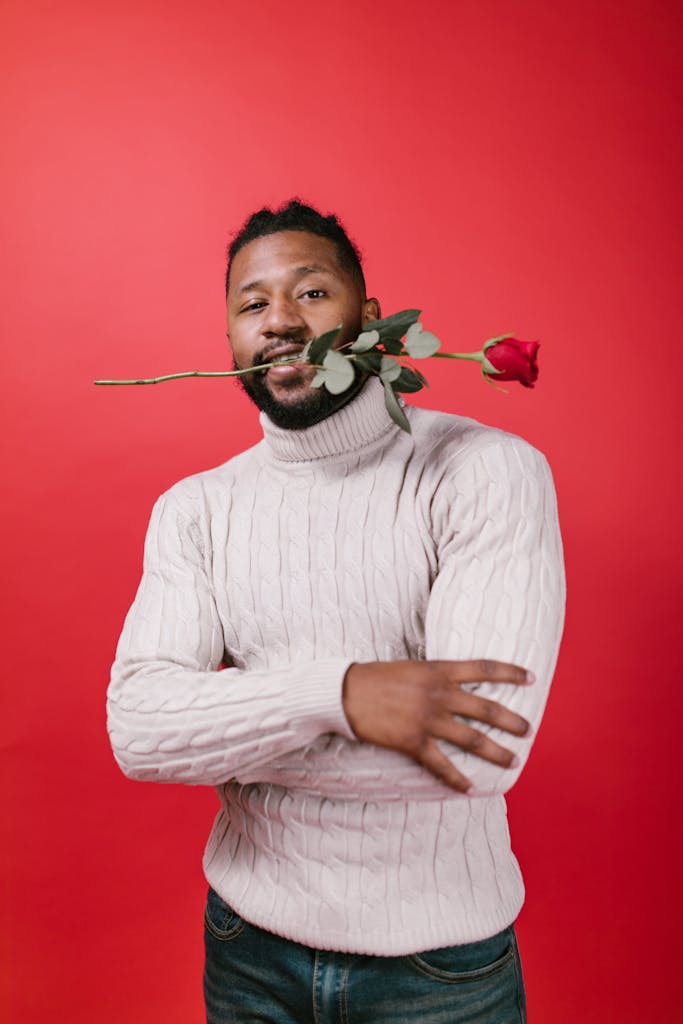 Charming man holding a rose in his mouth against a vibrant red backdrop, perfect for Valentine's imagery.