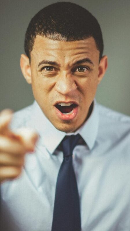 Close-up of an angry businessman in a tie expressing frustration and pointing.