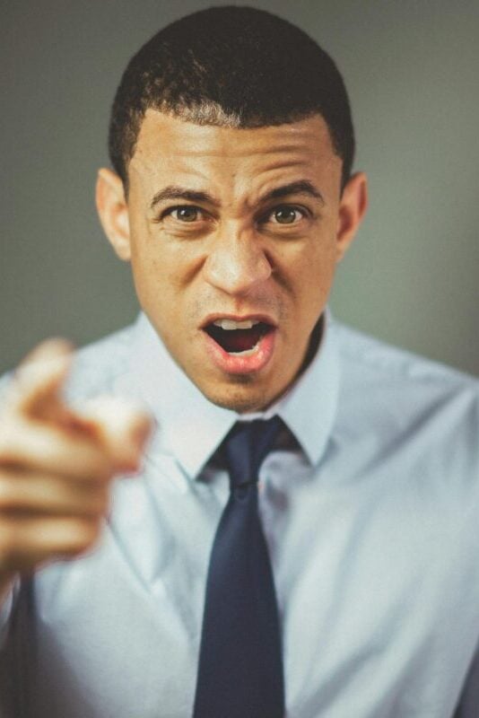 Close-up of an angry businessman in a tie expressing frustration and pointing.