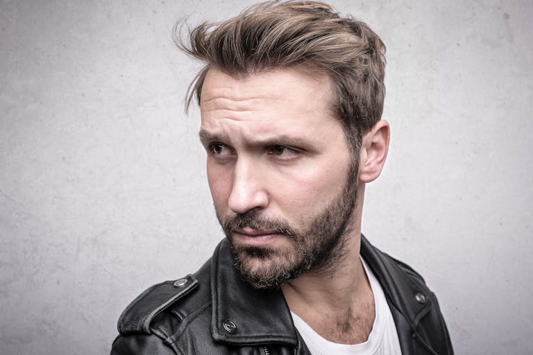 Close-up portrait of a bearded man in a leather jacket with a pensive expression.