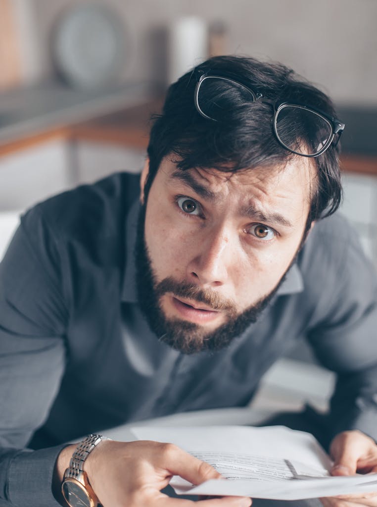 Portrait of an astonished man with a beard holding documents inside an office.