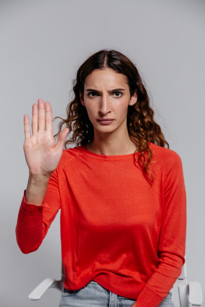 Serious woman with curly hair in a red top gesturing stop inside a studio.