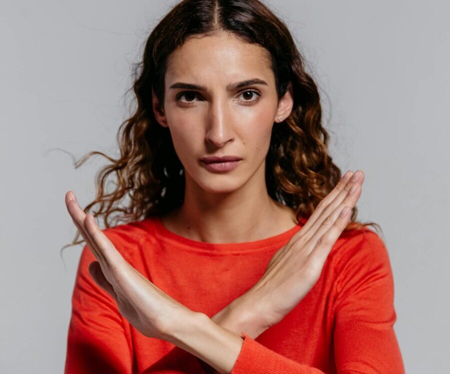 Woman in red shirt crossing arms in stop gesture, studio indoor portrait.