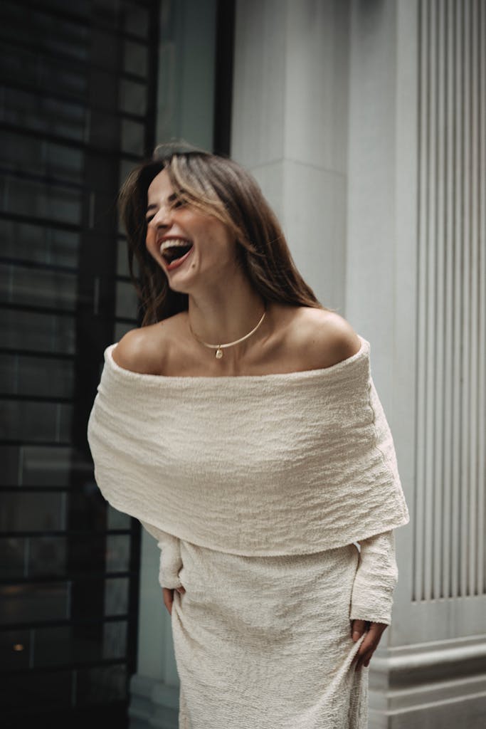 Woman laughing in a stylish off-shoulder dress outdoors.