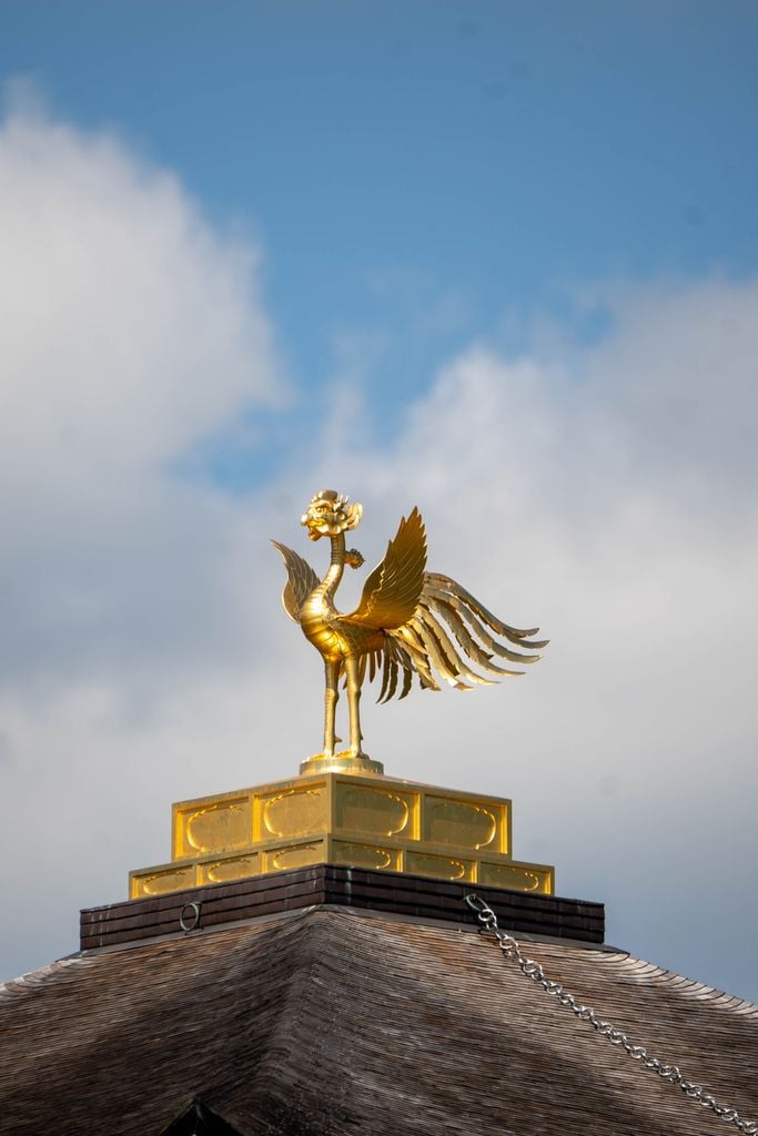 A golden phoenix statue decorates the roof, set against a clear blue sky.