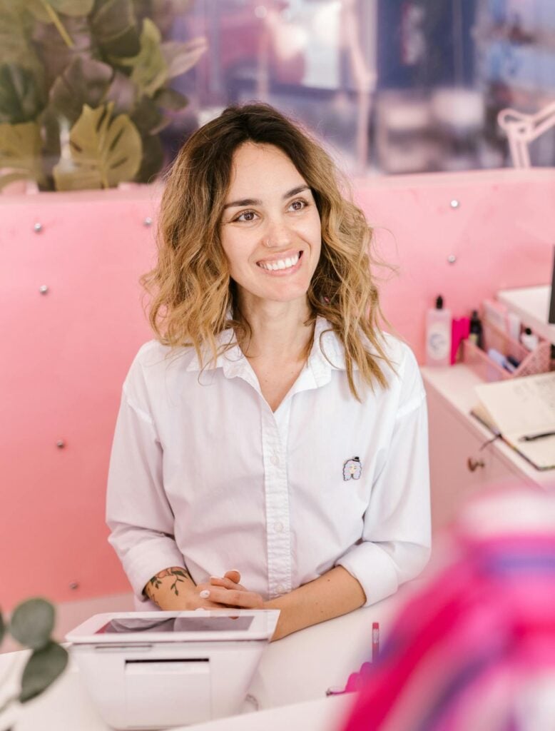 Smiling receptionist at a salon front desk, welcoming clients with a friendly demeanor.