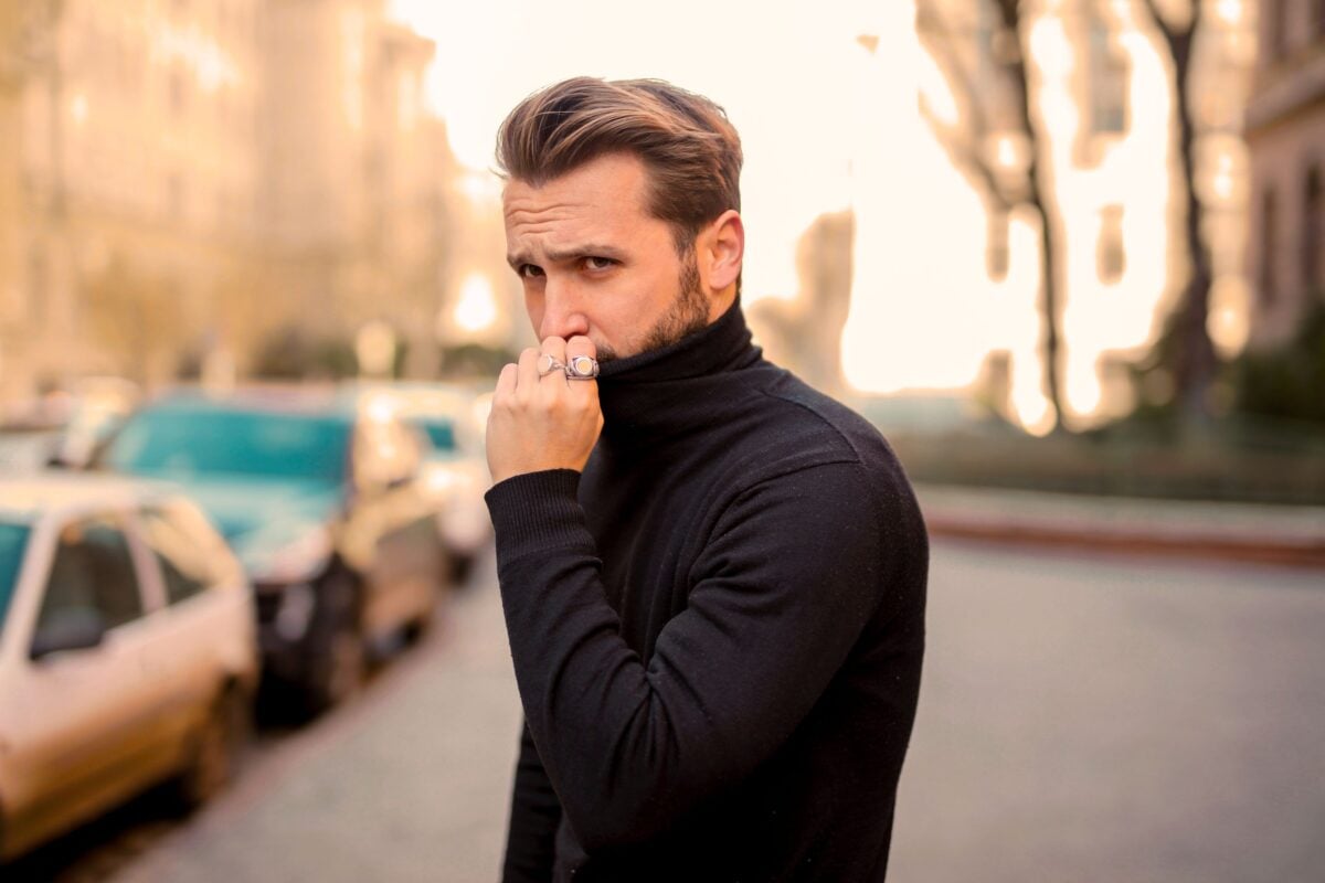 Stylish man stands outdoors with serious expression in city setting.