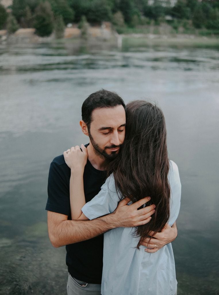 A couple shares an intimate embrace by a serene lakeside, evoking feelings of love and tranquility.