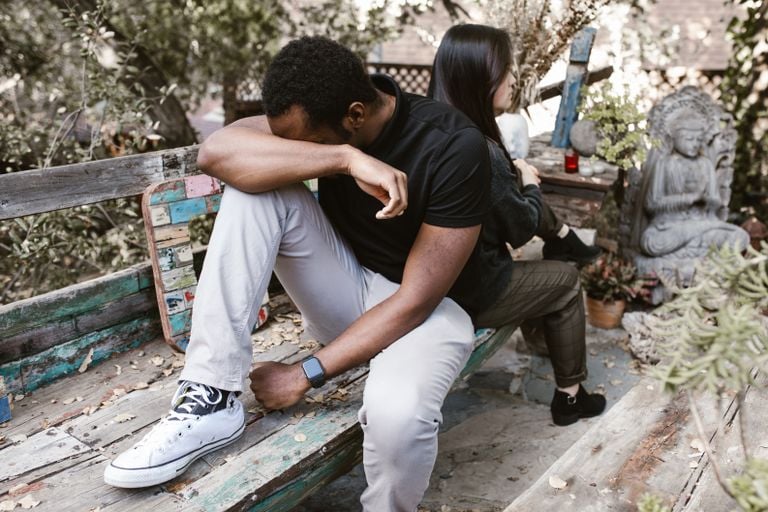 A couple sitting back to back in a garden, expressing sadness and tension.
