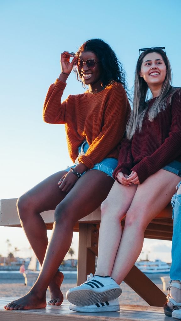 Two young women sitting at the beach laughing and enjoying a sunny day together.
