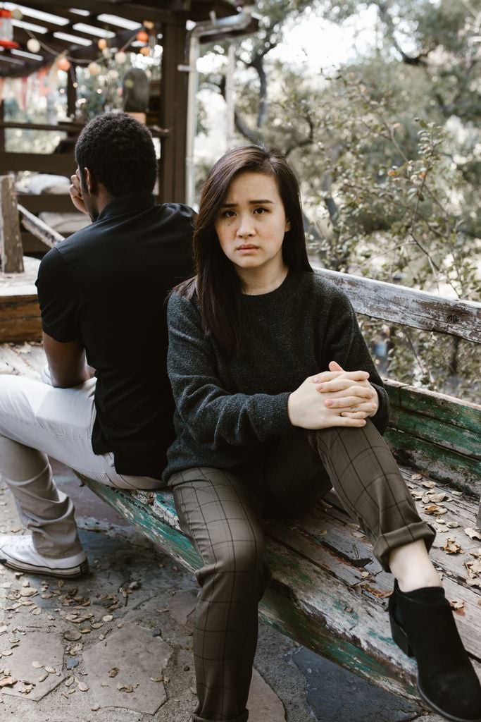 A couple sits back-to-back on a bench, expressing tension and conflict.