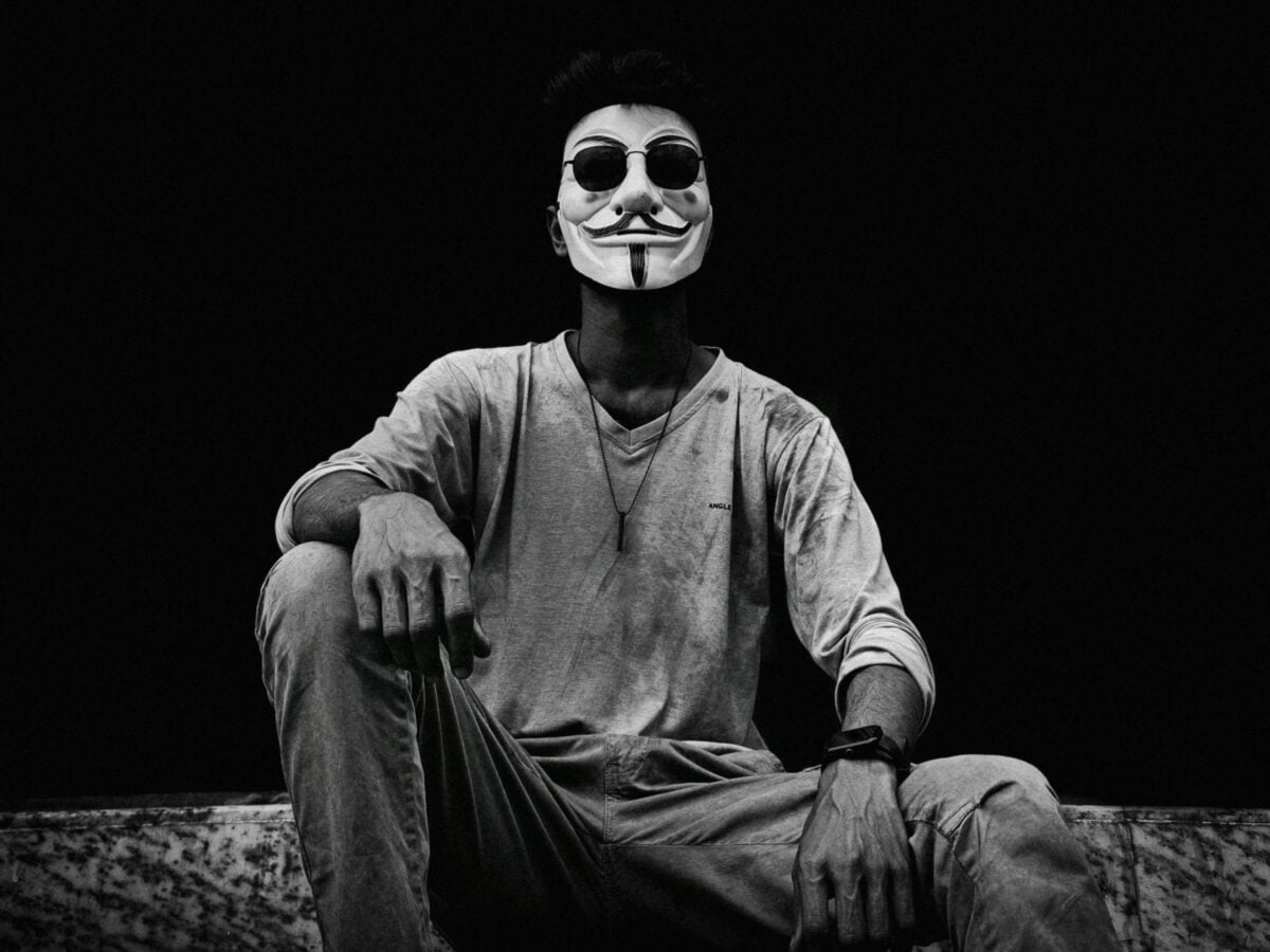A dramatic black and white portrait of a man in a Guy Fawkes mask.