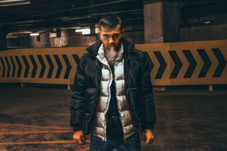 A man in a puffer jacket smoking inside an underground parking garage at night.