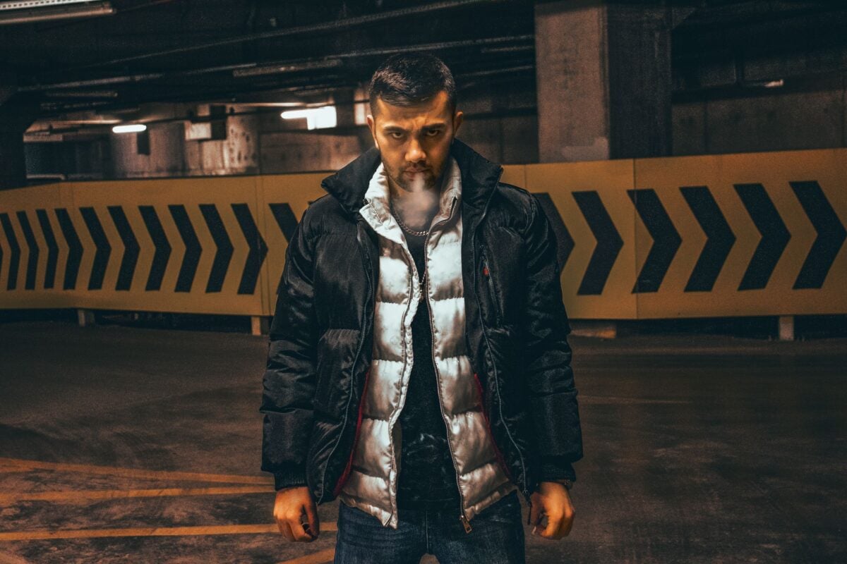 A man in a puffer jacket smoking inside an underground parking garage at night.