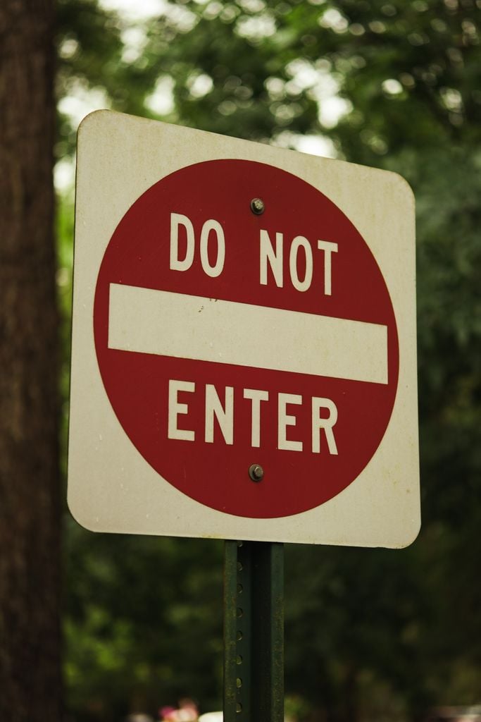 A prominent red and white Do Not Enter sign amidst green foliage, outdoors.