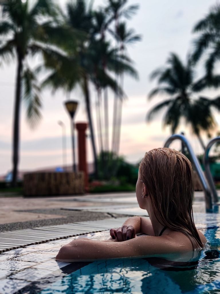 A woman enjoys leisure time in a swimming pool surrounded by palm trees in Malaysia.