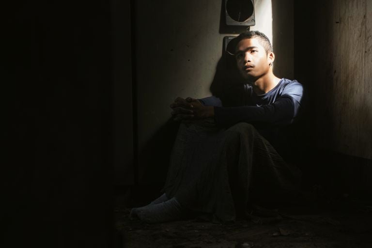 A young man sits alone in a dimly lit room, deep in thought.