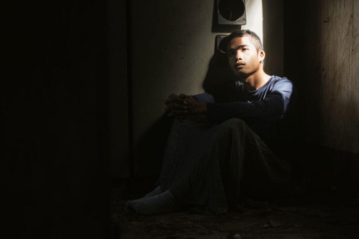 A young man sits alone in a dimly lit room, deep in thought.