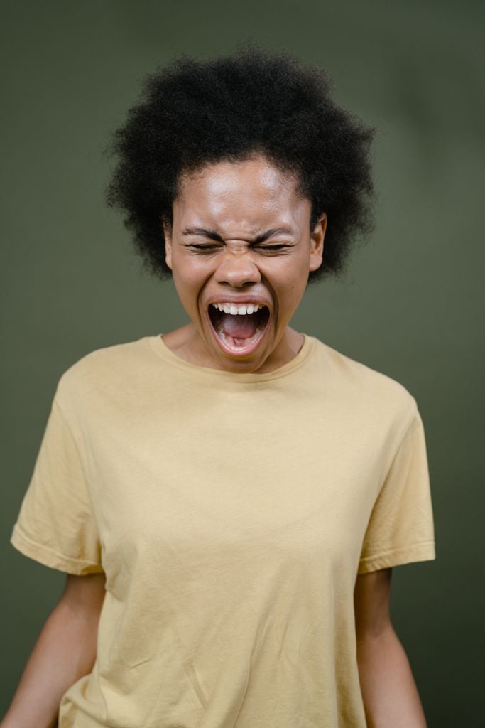 African American woman with afro hair expressing intense emotion by shouting.