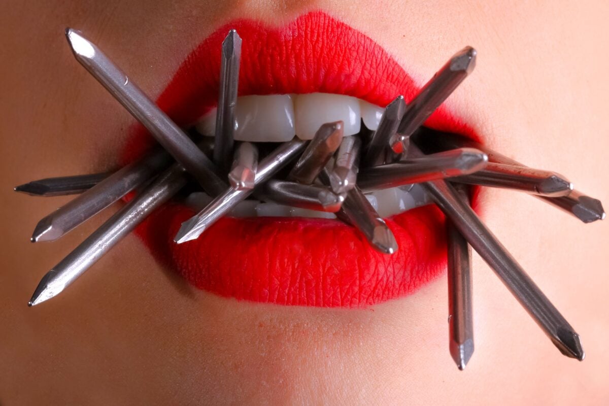 Artistic close-up of red lips biting metal spikes, contrasting beauty and strength.