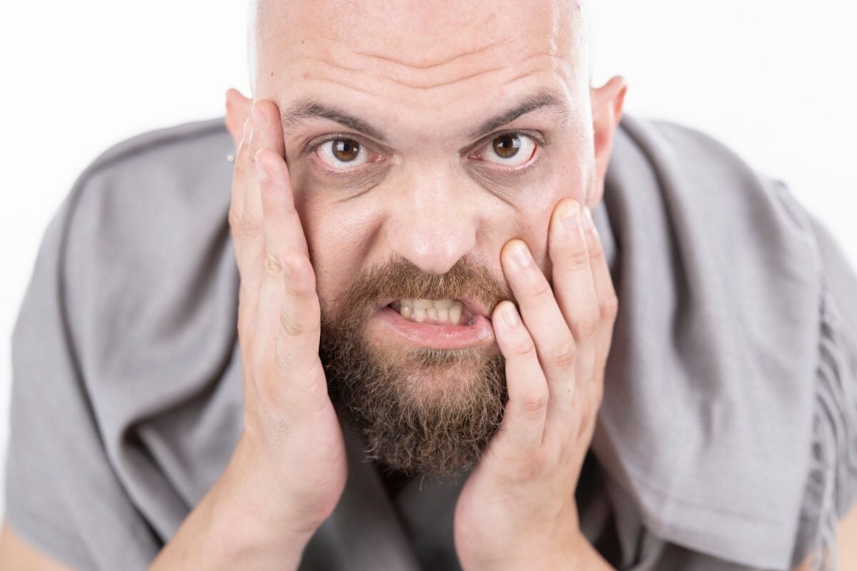 Close-up of a bearded man showing frustration with hands on face.