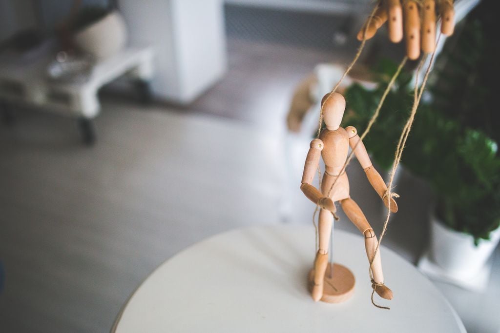 Close-up of a wooden marionette controlled by strings indoors. Artistic representation of control and manipulation.