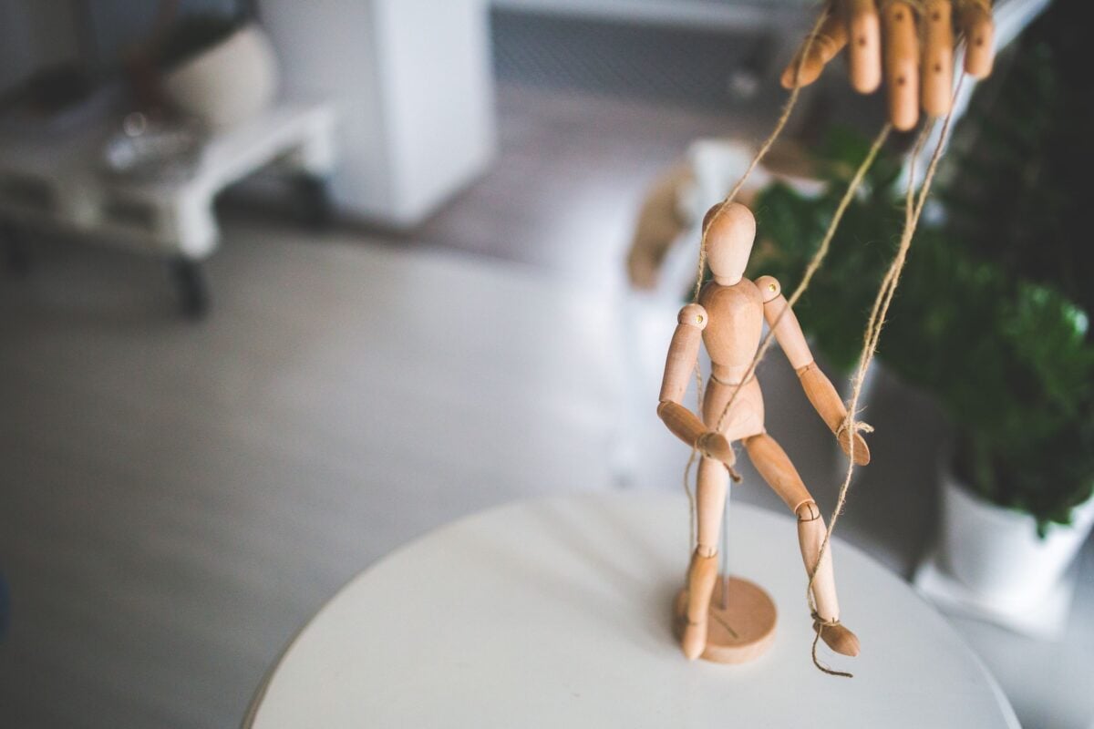 Close-up of a wooden marionette controlled by strings indoors. Artistic representation of control and manipulation.