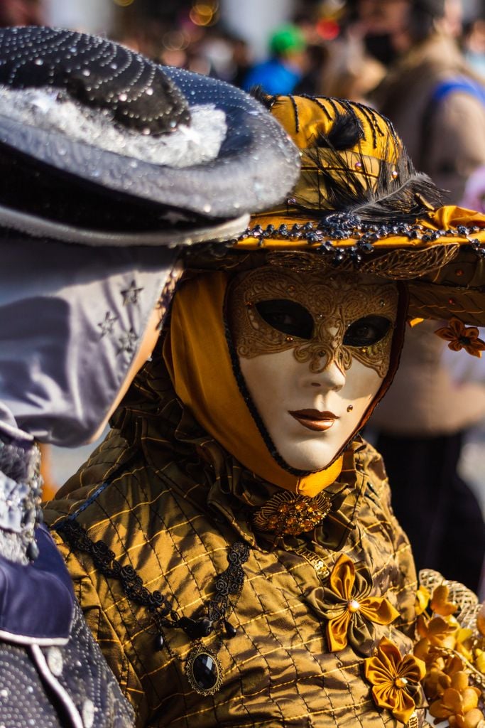 Close-up of an ornate masked figure in yellow costume at Venice Carnival, capturing the essence of Venetian tradition.