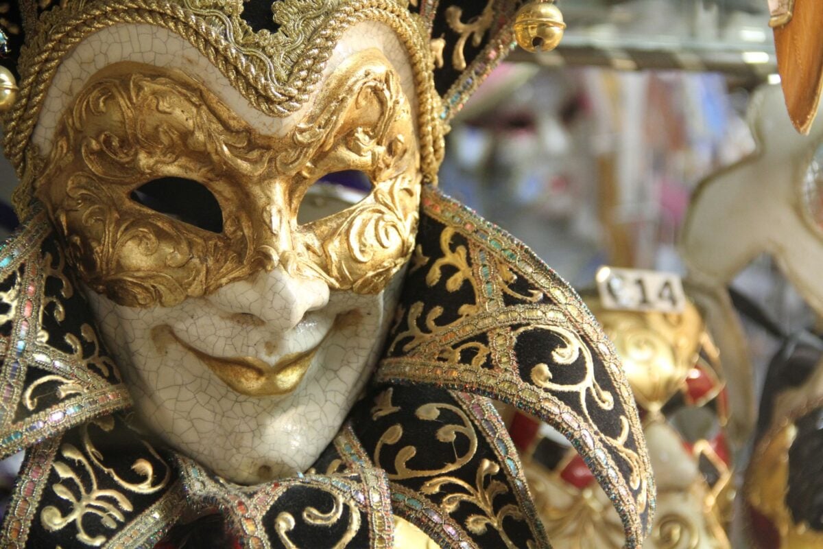Closeup traditional elegant Venetian mask with golden ornaments hanging in vitrine of shop during carnival