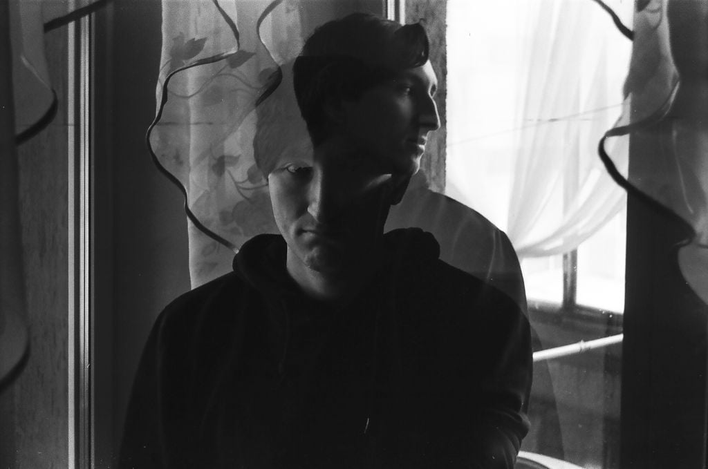 Double exposure portrait in black and white featuring a man by a window with curtains.