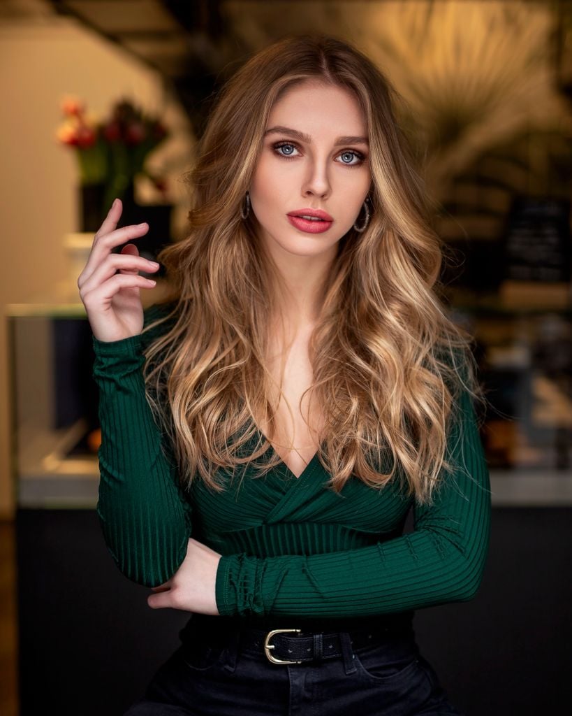 Elegant and attractive woman with long blonde hair posing indoors in a green top.