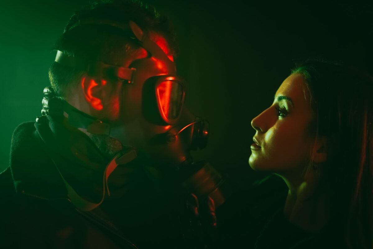 Intense studio portrait of a man in gas mask confronting a woman under dramatic lighting.