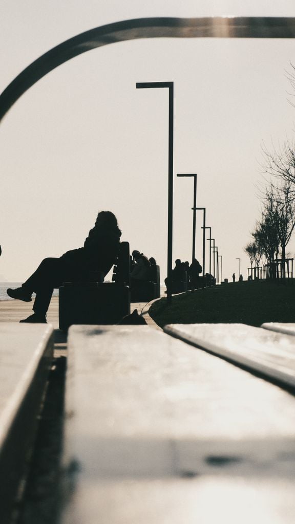 Silhouetted individuals enjoy a peaceful moment on an outdoor urban bench during the day.