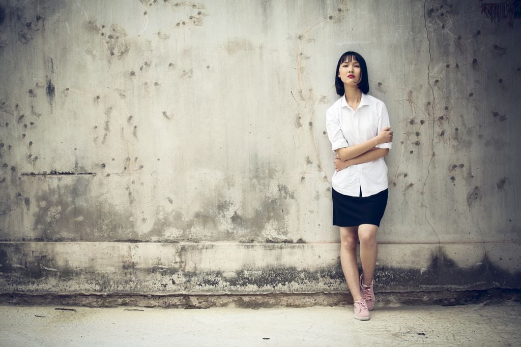 Stylish portrait of a woman posing against an aged concrete wall, showcasing modern fashion outdoors.