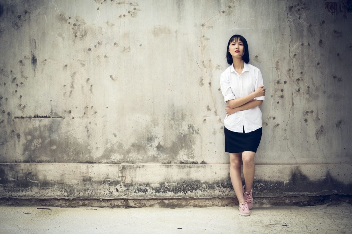 Stylish portrait of a woman posing against an aged concrete wall, showcasing modern fashion outdoors.
