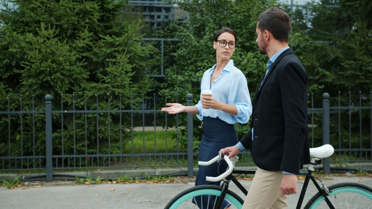 Two business professionals walking and discussing outside with a bicycle.