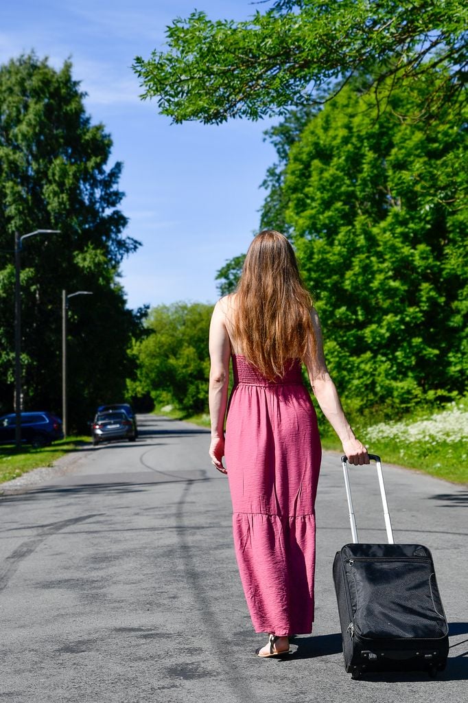 Woman in pink dress walking with suitcase on sunny day in Tallinn, Estonia.