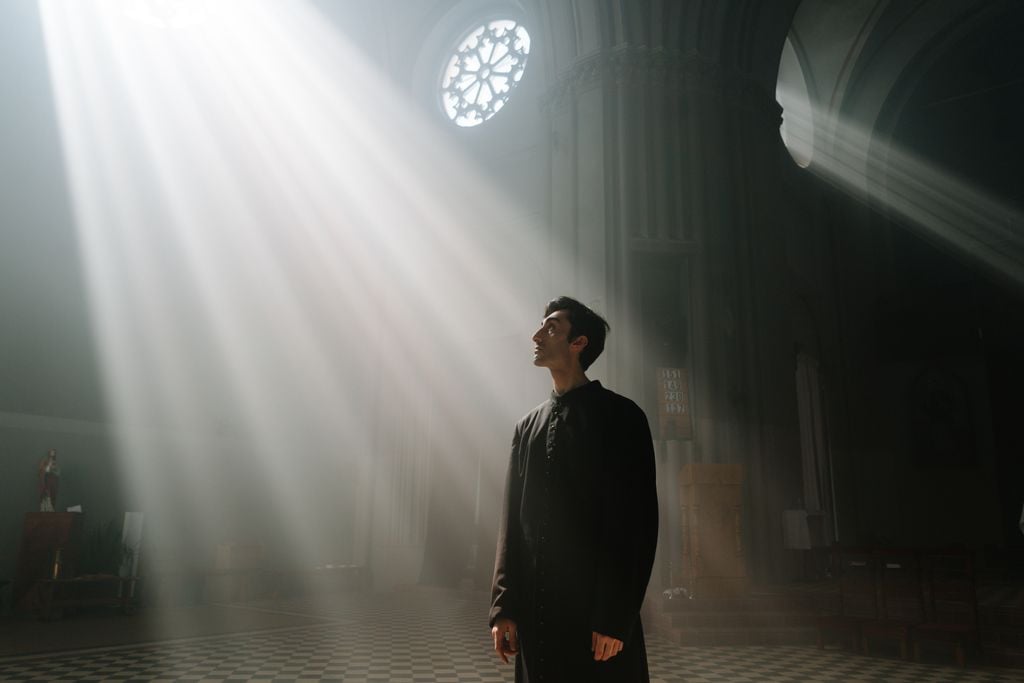 A priest standing in sunlight rays inside a cathedral, symbolizing faith and divinity.