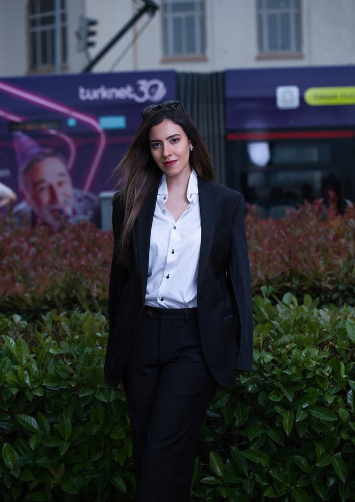 A professional woman in a suit stands confidently in an urban environment.