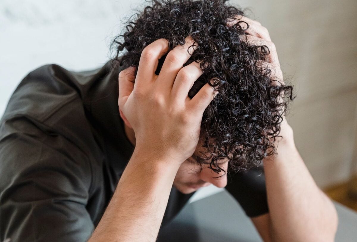 An adult with curly hair looks frustrated, holding head in hands.