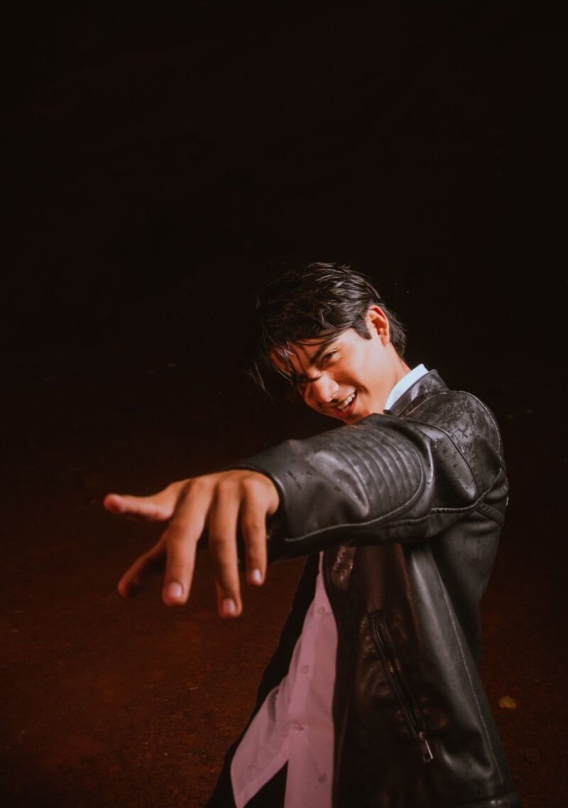 Portrait of a stylish young Hispanic man in a leather jacket, posing outdoors at night.
