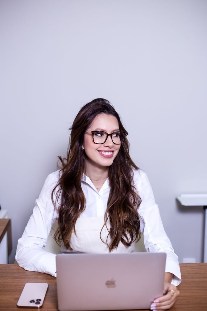 Smiling woman in glasses using a laptop at a desk, displaying a professional work environment.