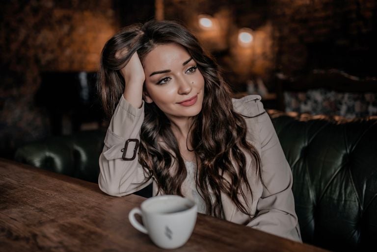 Young woman with long hair enjoys a tranquil moment in a cozy café with a cup of coffee.