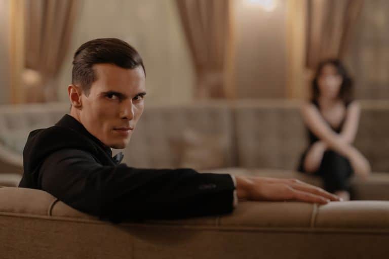 A stylish man in a suit relaxing on a sofa in an elegant room with blurred background.