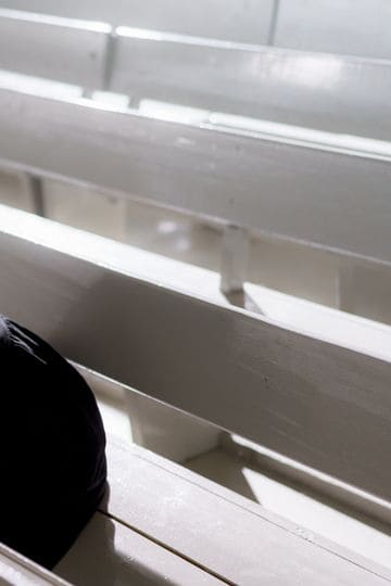 A woman in black clothes leans over pews, grieving alone in an empty church.