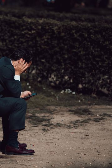 A worried businessman sits on a park bench in Madrid, holding a smartphone. Captured outdoors in natural light.