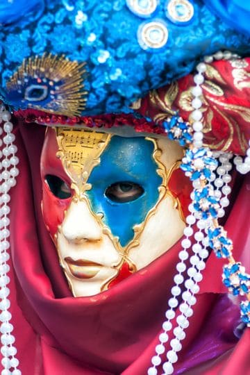 Close-up of a colorful Venetian carnival mask with ornate beads and rich fabrics.